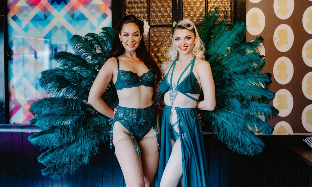 Two burlesque performers posing in teal coloured feathery costumes. 